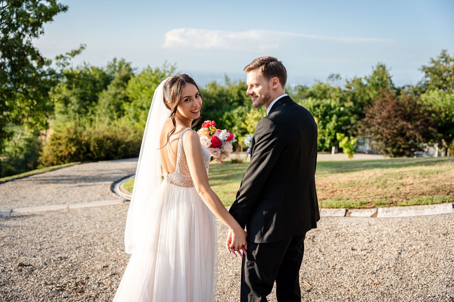 Bride and groom holding hands on a gravel path surrounded by lush greenery on wedding day.