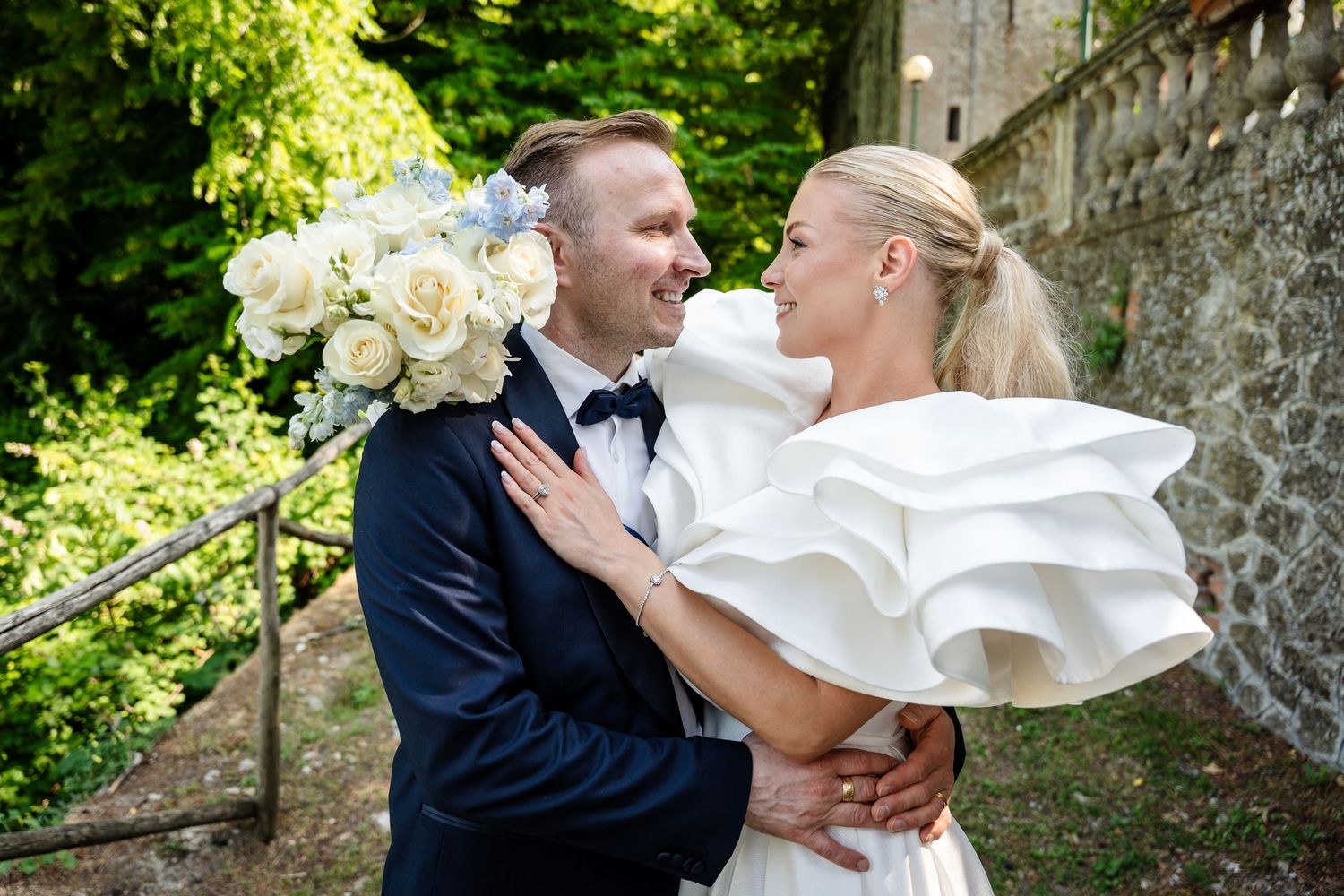 A romantic wedding couple shares intimate moments in a lush garden setting near a stone wall.