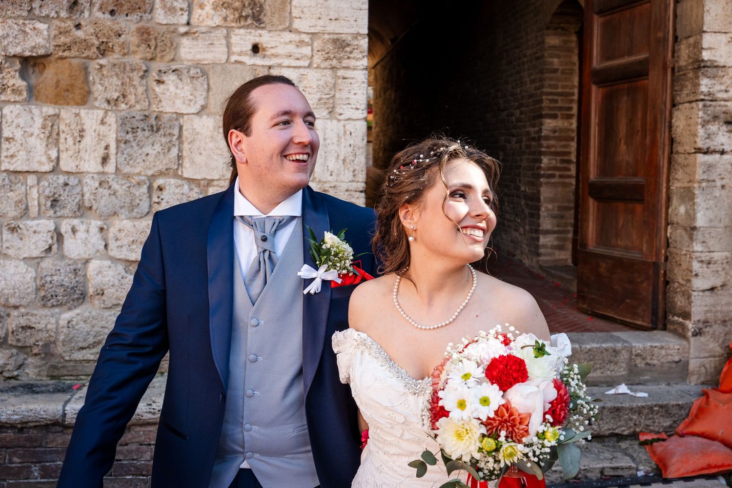 Smiling bride and groom posing together outside a rustic stone church on their wedding day.