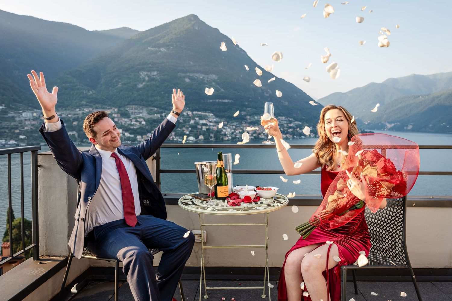 Couple celebrates with confetti on a lakeside terrace overlooking mountains during sunset in Switzerland.