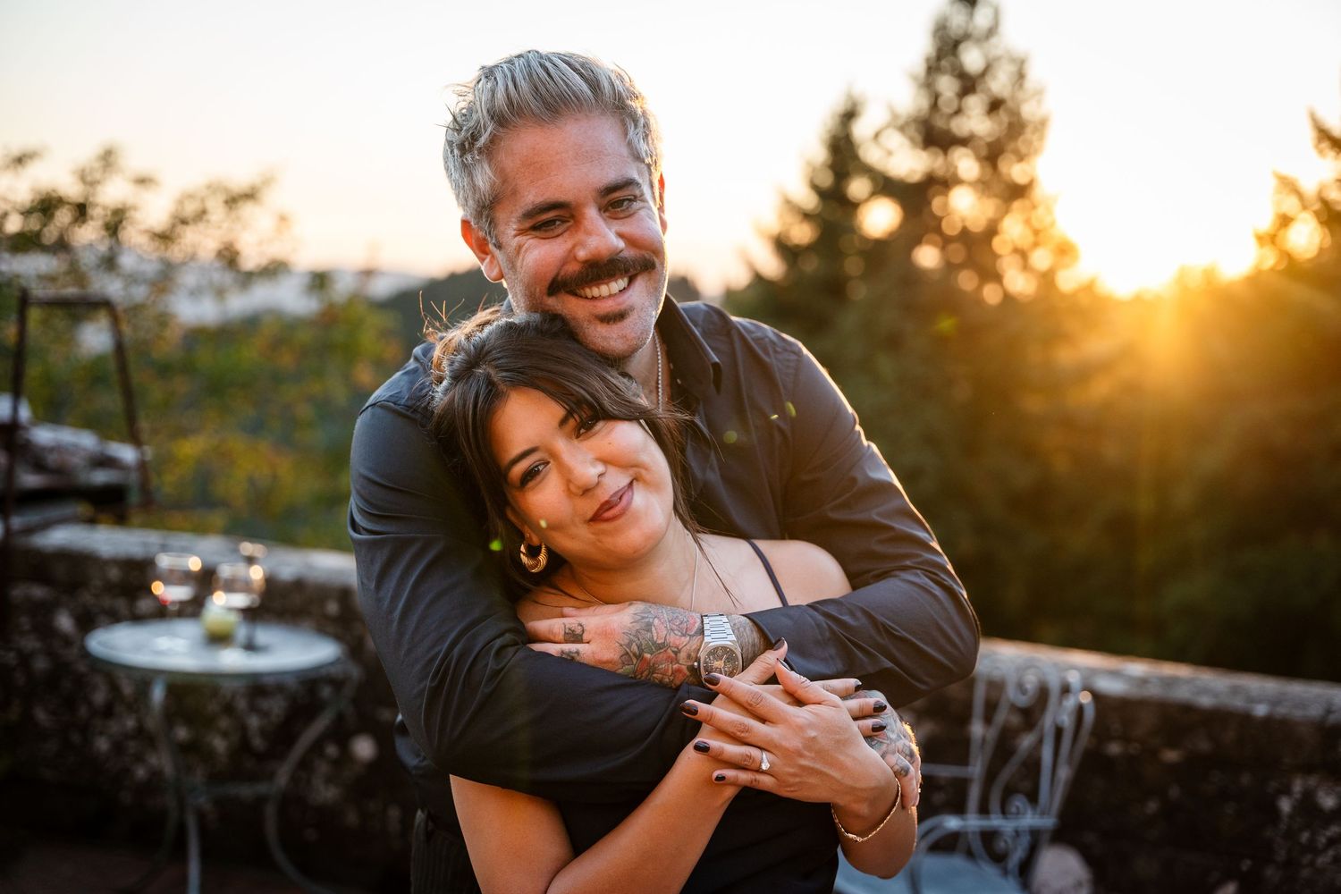 Couple embraces lovingly at outdoor venue during golden sunset hour with glowing warm light in background.