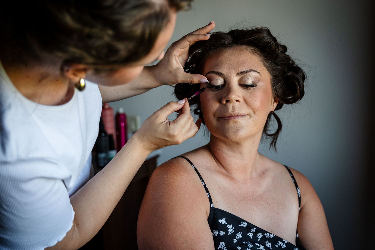 Makeup artist applies eyeshadow to client wearing polka dot dress during professional beauty session.