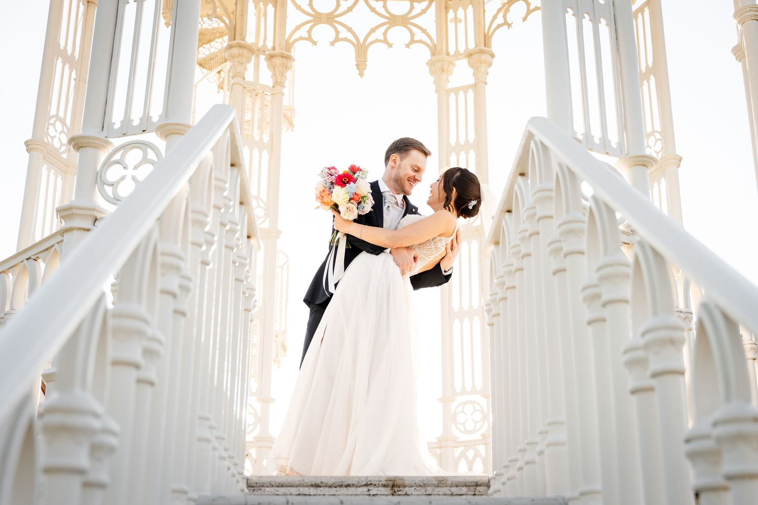 Bride and groom embracing romantically on white ornate chapel steps.