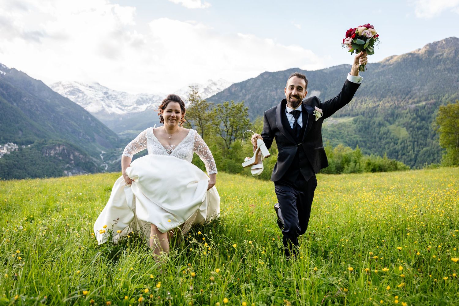 A couple celebrates their wedding day in a scenic mountain meadow filled with wildflowers and rolling hills.