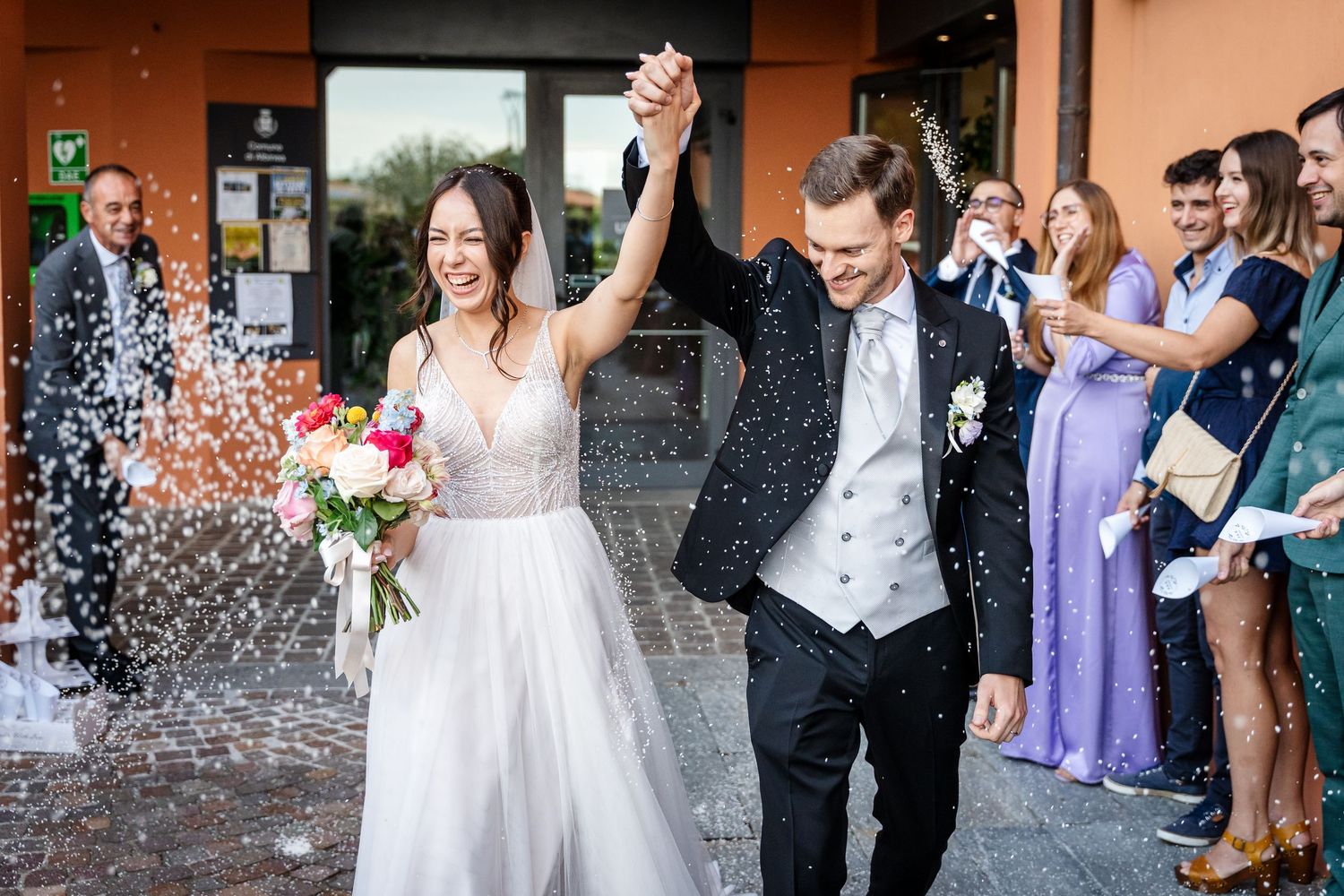 Wedding guests toss rice confetti over the newlyweds as they exit their ceremony in joyful celebration.