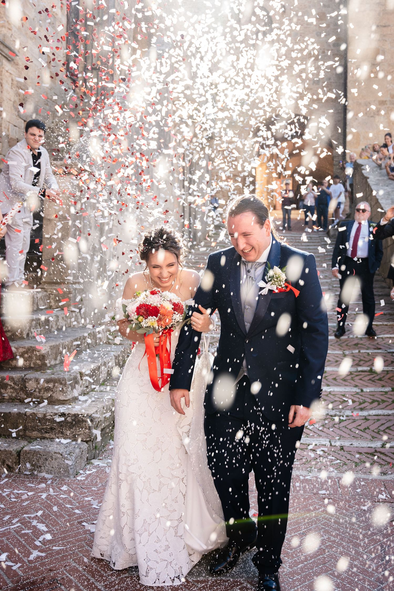 Joyful newlyweds exit church amid shower of white confetti on historic Italian stone steps.