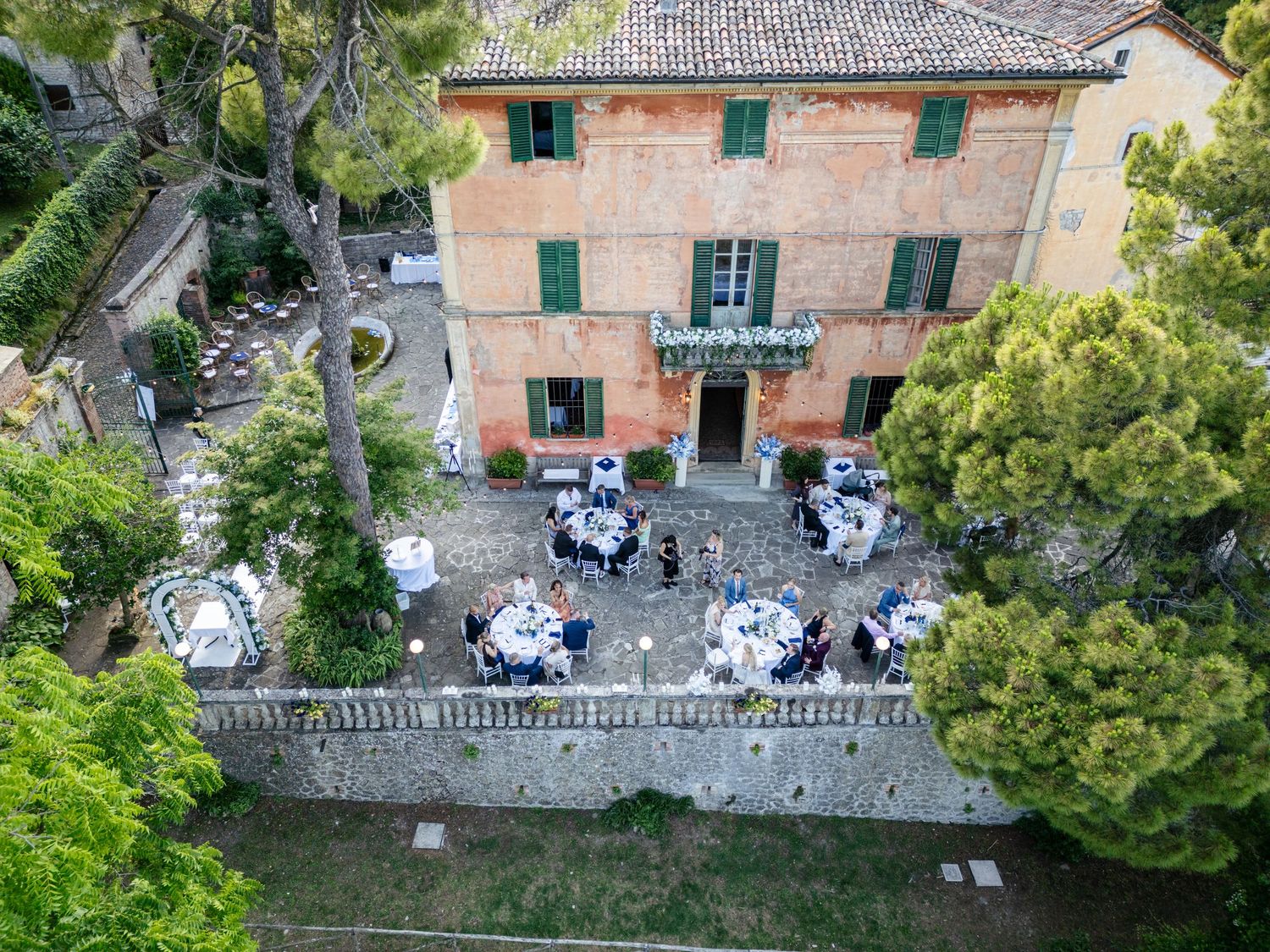 Aerial view of an Italian villa's outdoor dining setup with white tables arranged along a stone terrace wall.