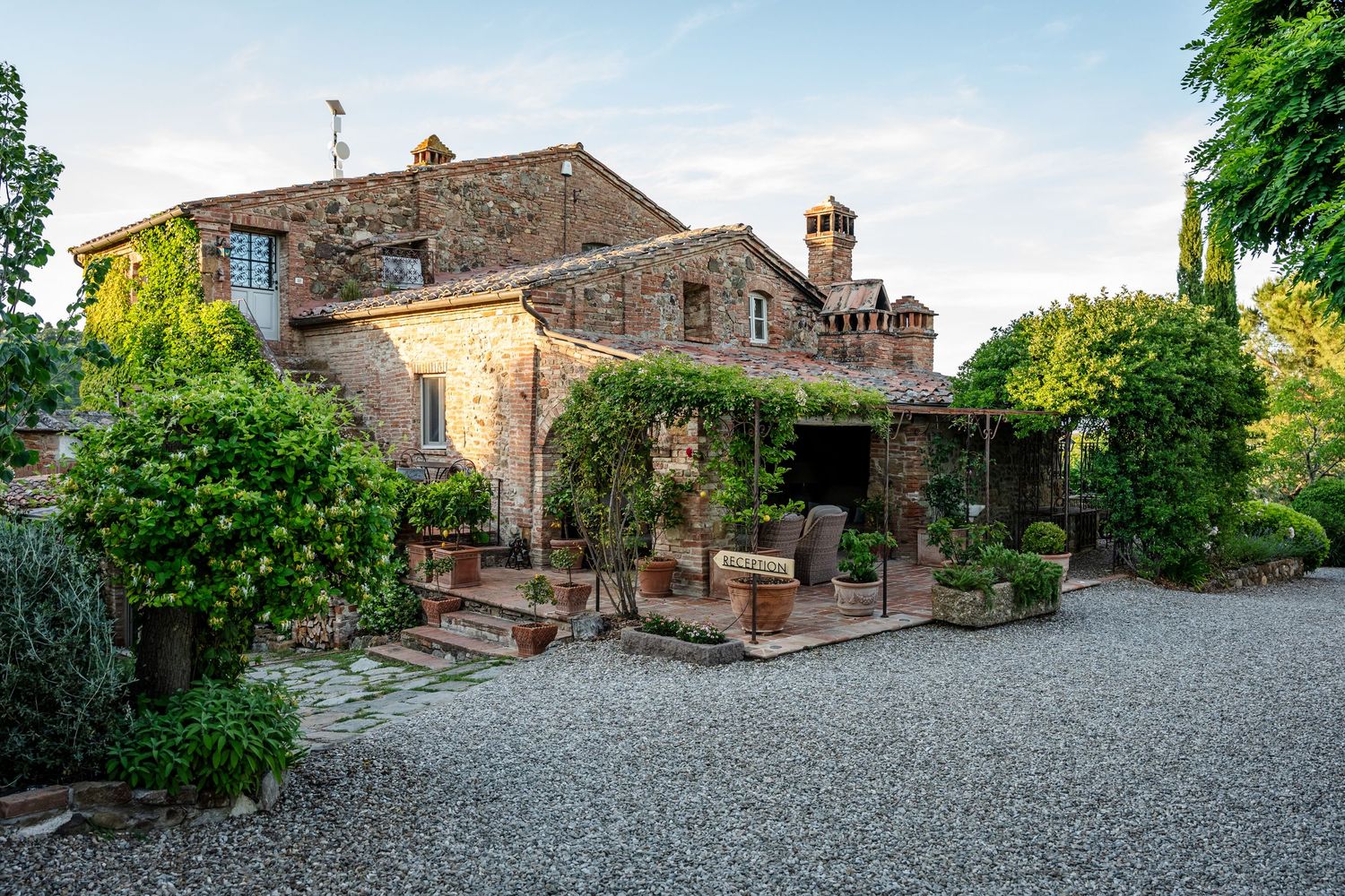 A panoramic view of a rustic stone villa and courtyard in the Tuscan countryside with lush green vegetation.
