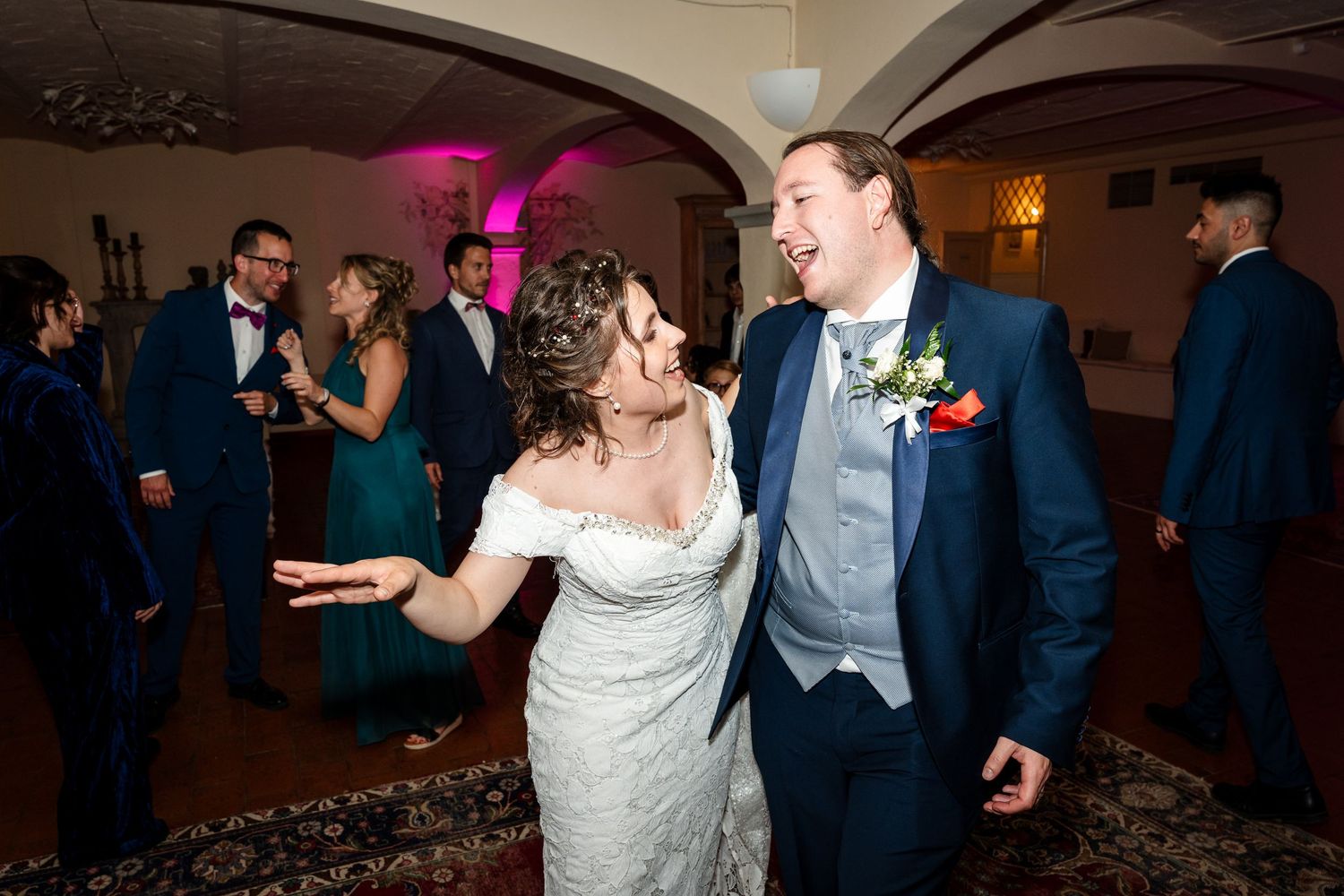 Happy bride and groom laugh together while dancing at lively indoor wedding reception celebration.