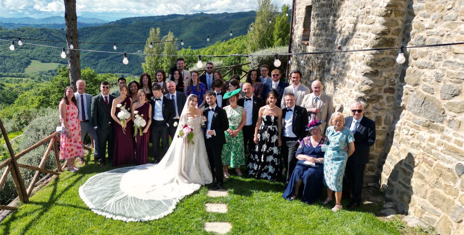 Wedding party posing together outdoors at a scenic Italian villa with lush green hills in the background.