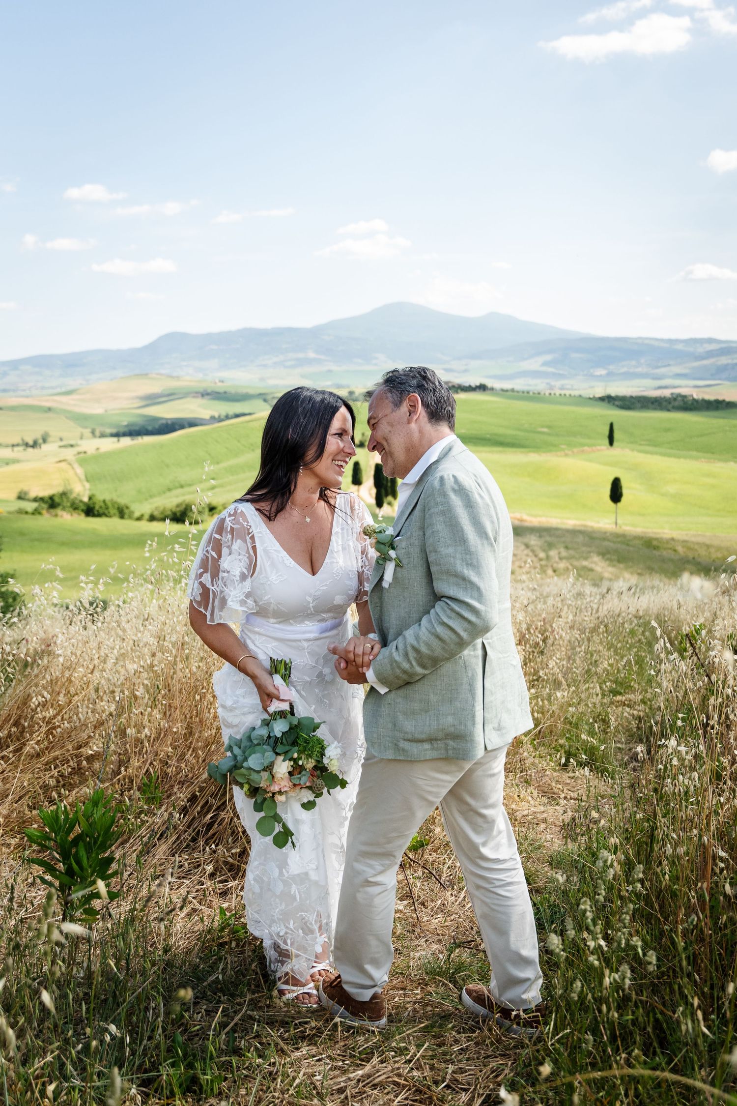 A couple shares intimate moments in a scenic Tuscan countryside with rolling hills and golden fields in the background.