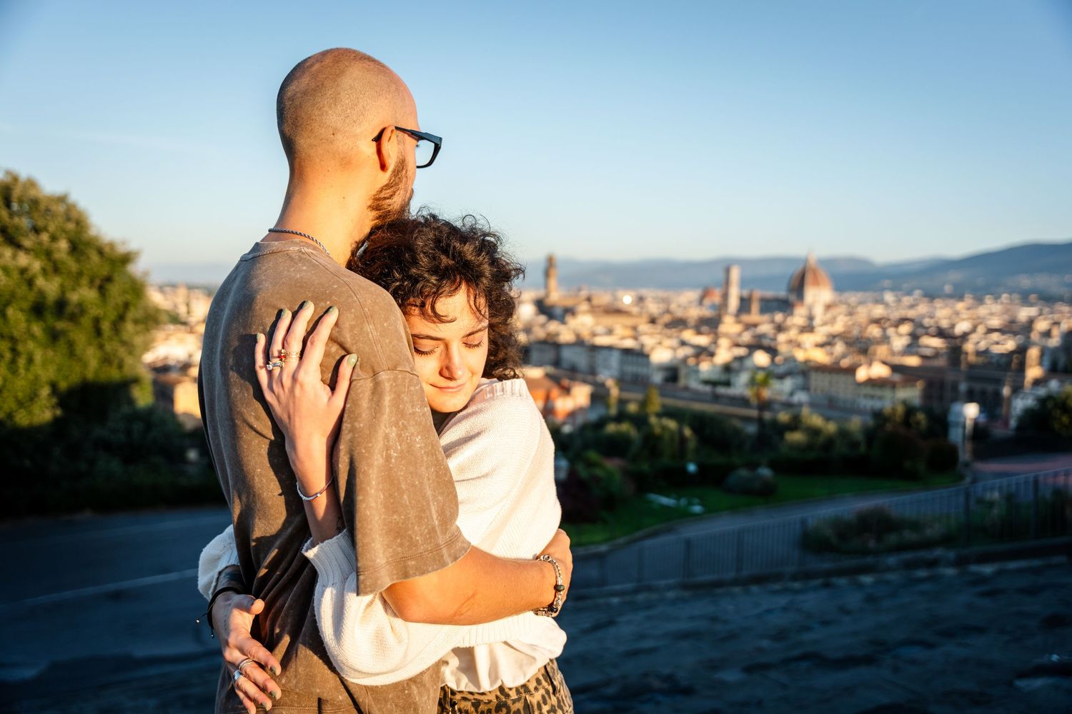 A couple embraces while enjoying a scenic panoramic view of Florence, Italy from Piazzale Michelangelo at sunset.