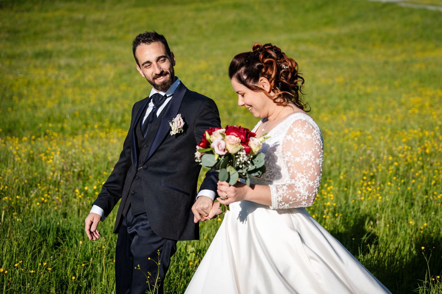 A couple shares a romantic moment in a green meadow filled with wildflowers during their wedding day celebration.