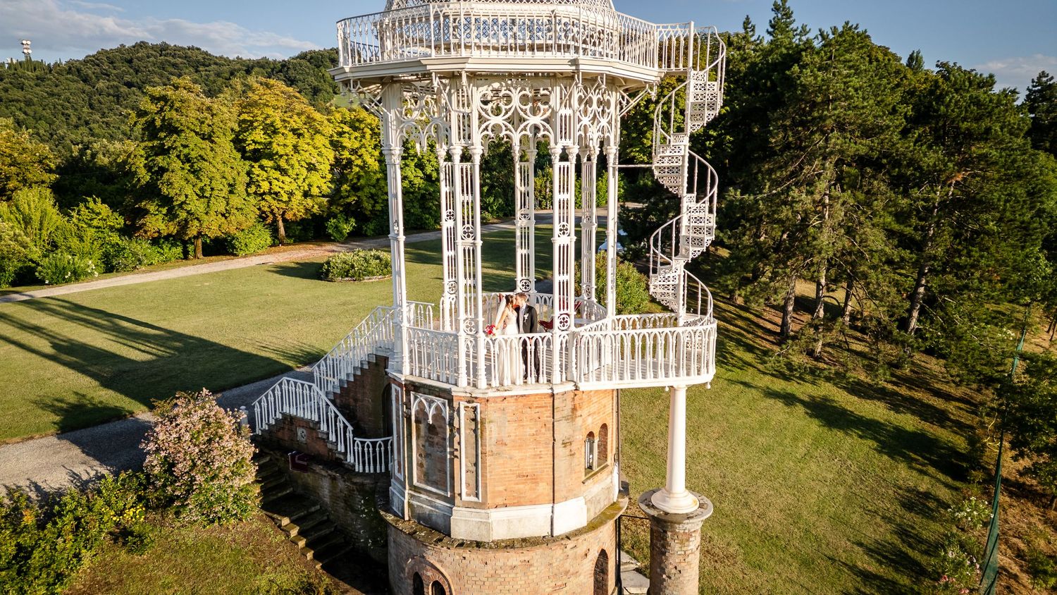 A panoramic view of a white gazebo structure in a lush green park setting with clear blue skies.