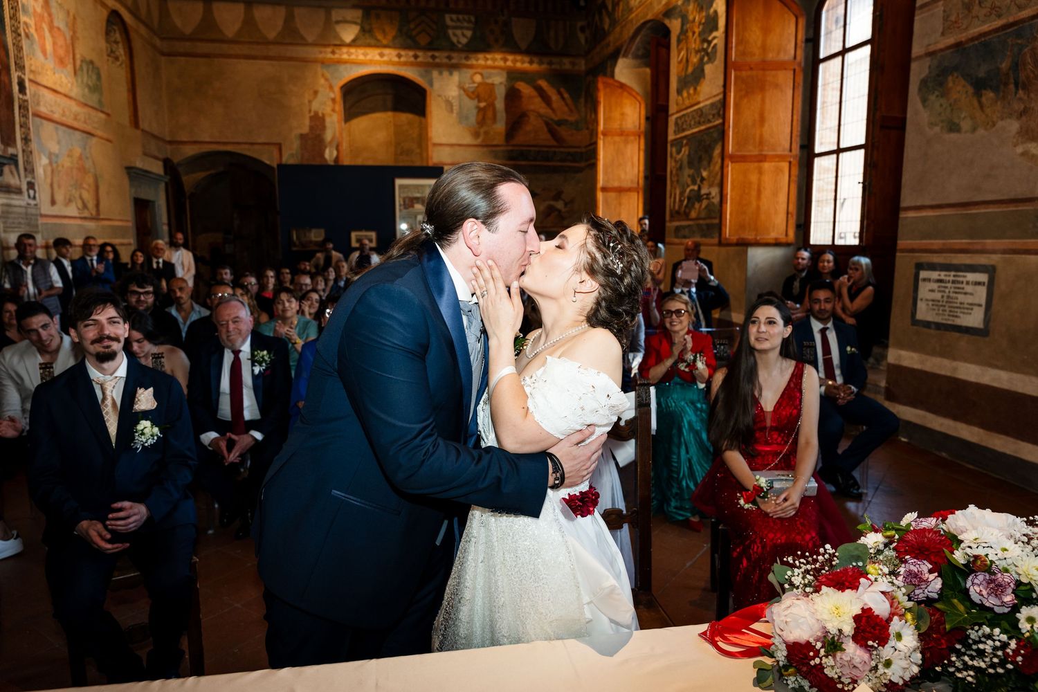 Bride and groom sharing a first kiss at the altar during their wedding ceremony in an ornate venue.