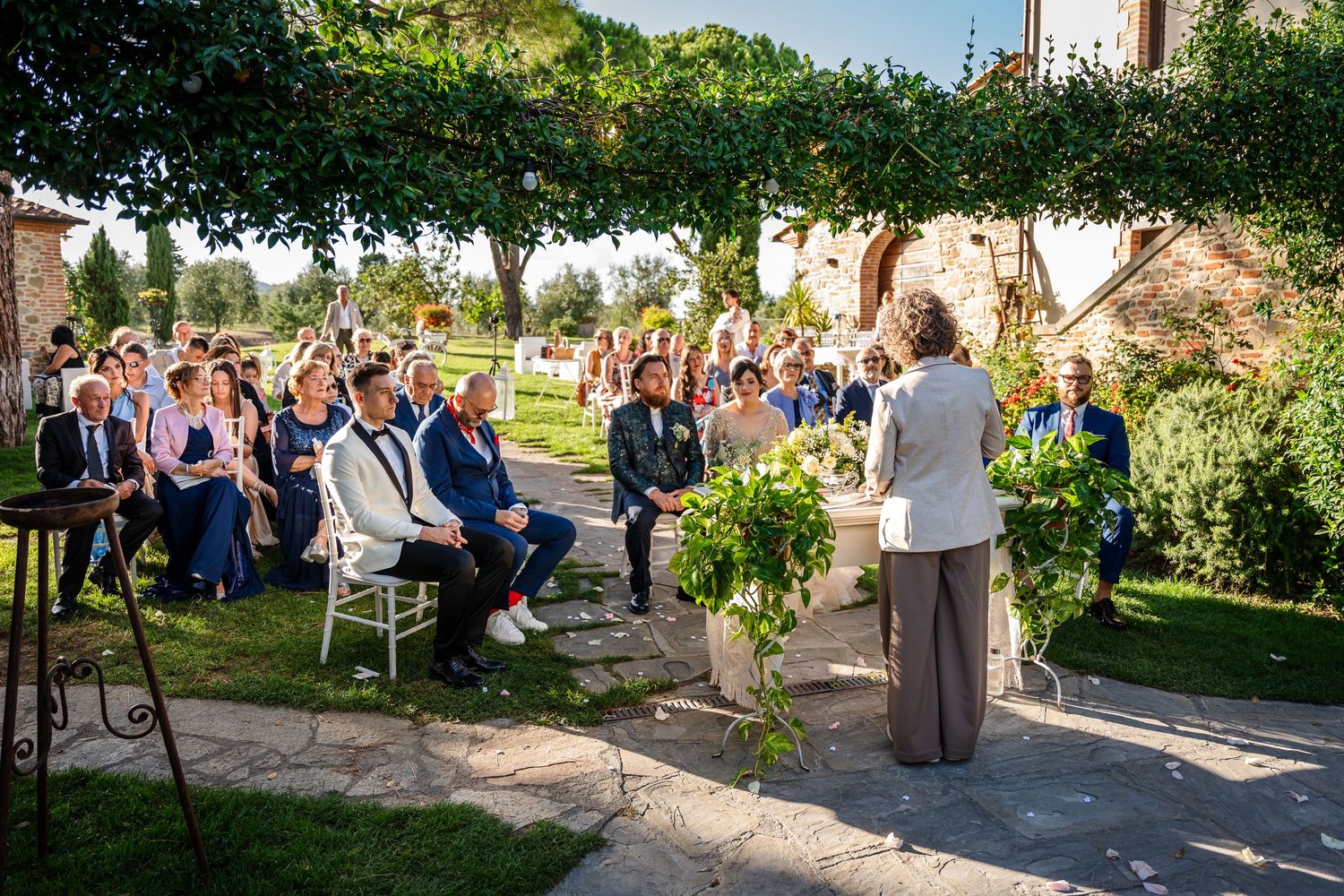 Wedding guests gather outdoors in a garden setting during a sunny afternoon celebration.