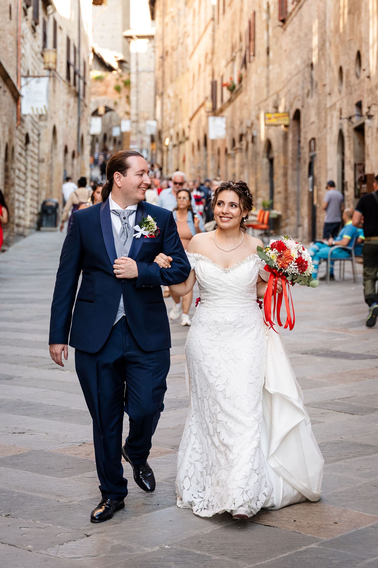 Happy newlyweds stroll arm in arm through a charming Italian cobblestone street after their wedding.