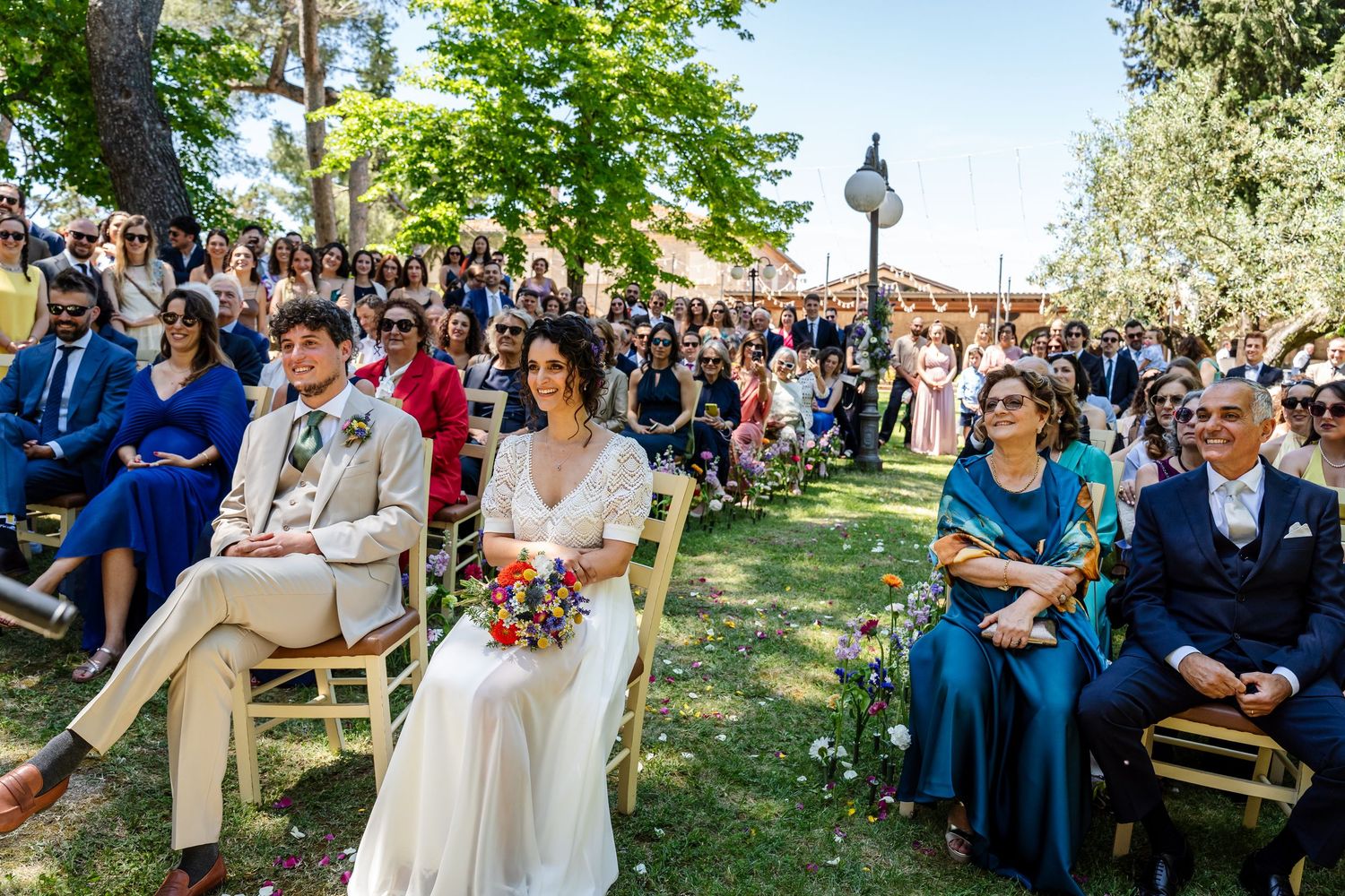 A row of wedding guests sitting on wooden benches during an outdoor garden ceremony.
