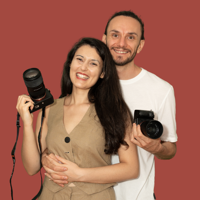 Professional photographers with cameras pose together in front of a red backdrop during a studio photoshoot.