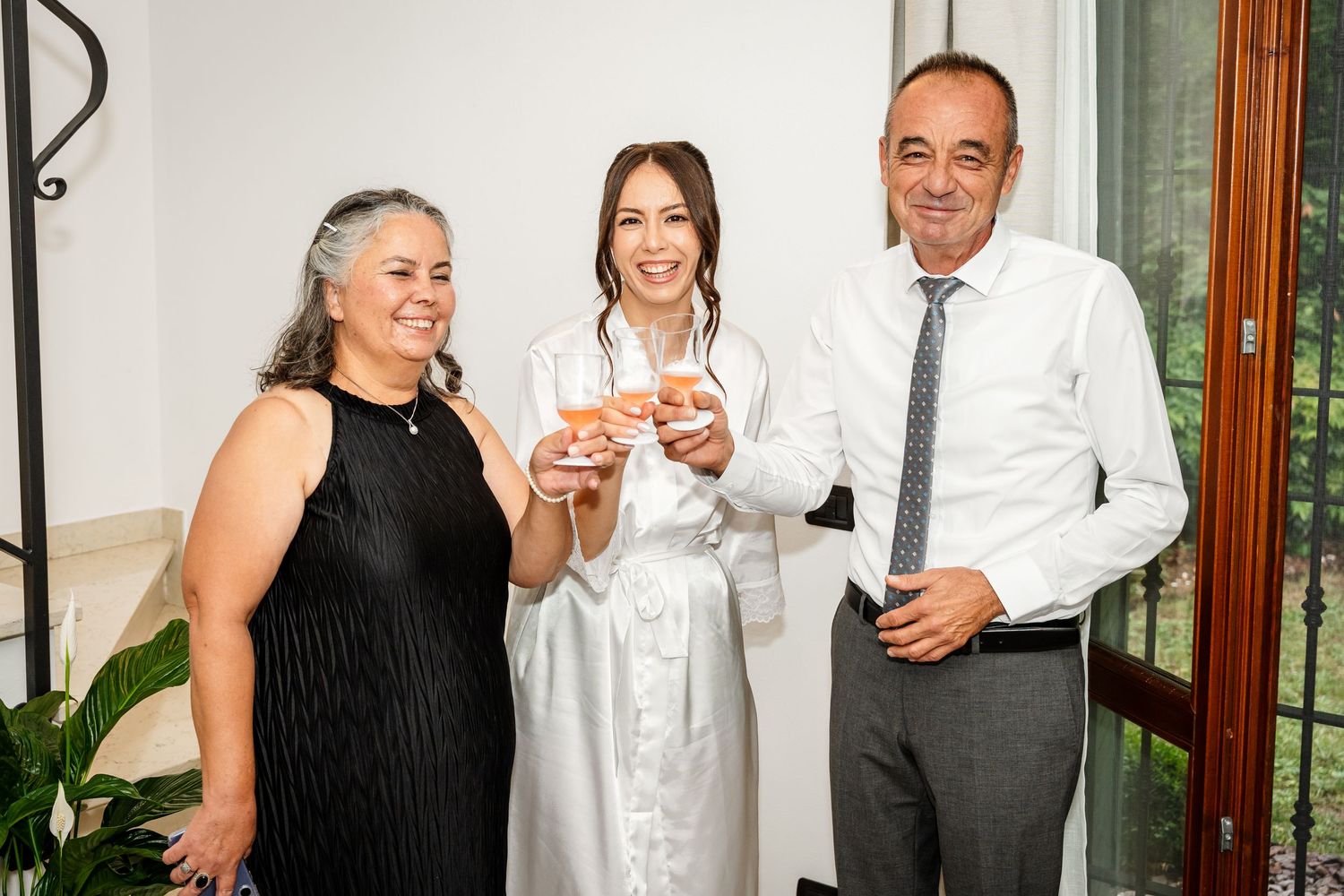 Bride in white dress toasting champagne with parents during wedding celebration indoors.