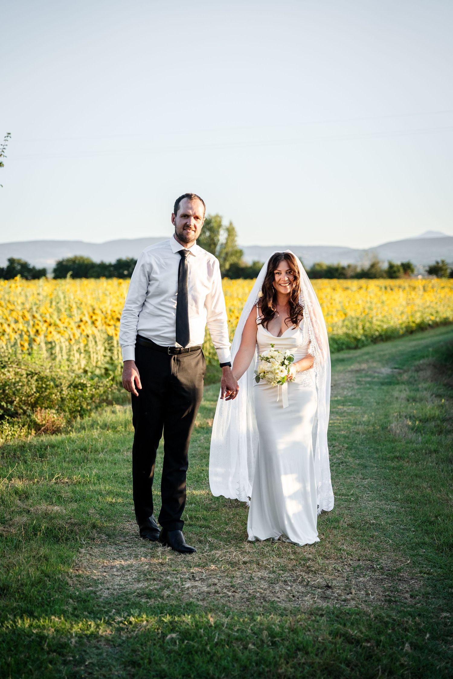 Bride and groom holding hands in front of a sunflower field on their wedding day.