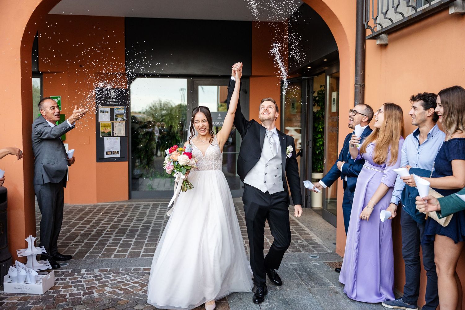 Joyful bride and groom exit wedding venue as guests celebrate with confetti and champagne.