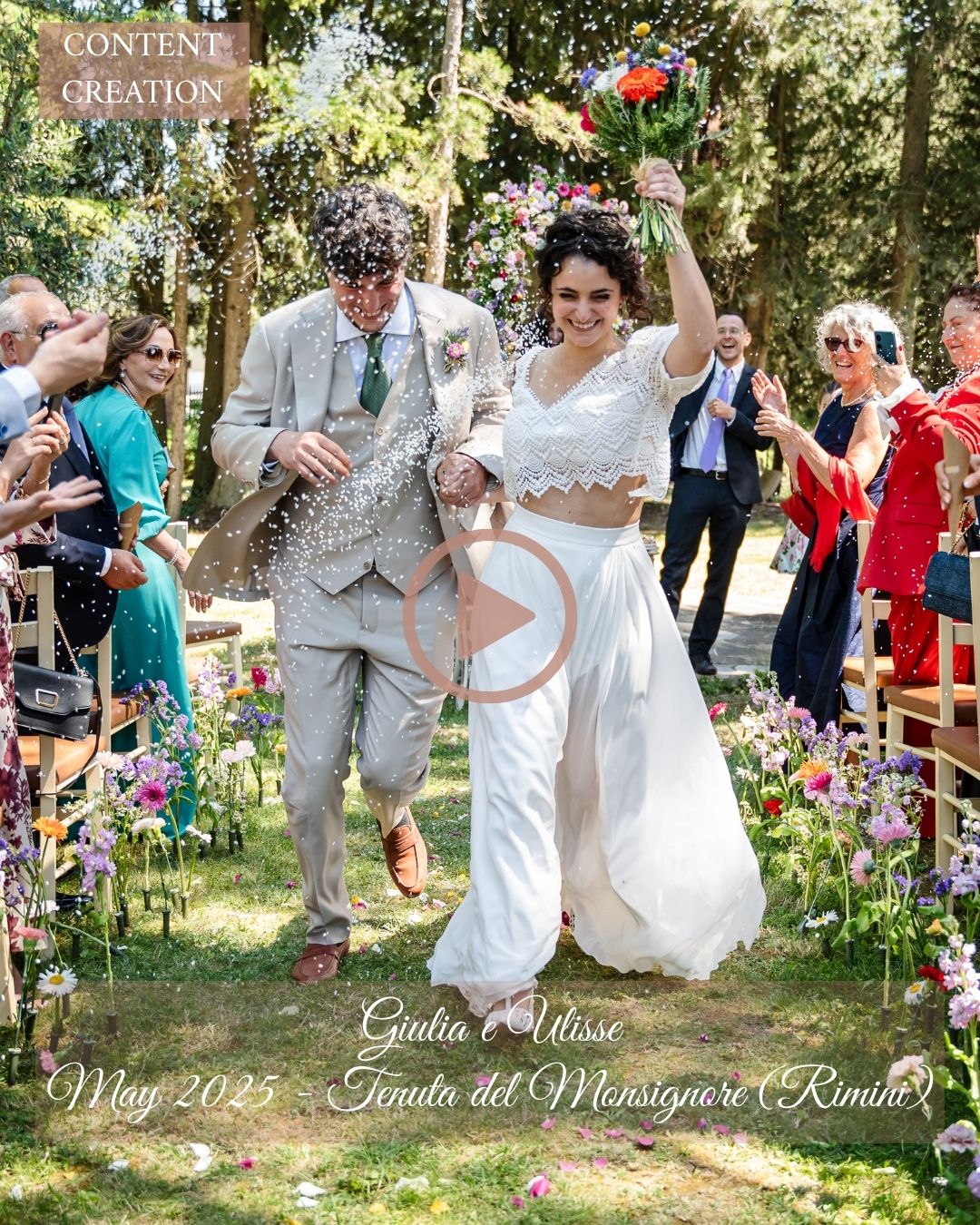 A joyful outdoor wedding celebration with guests jumping and dancing together in a garden setting surrounded by flowers.