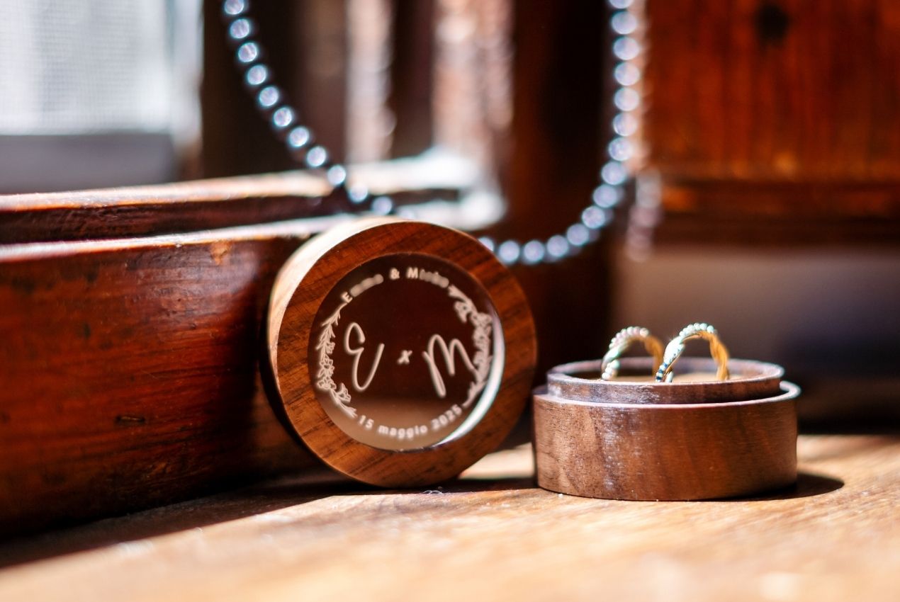 Personalized wooden wedding ring box with engraved initials and two rings resting on top, placed on a rustic wooden surface.