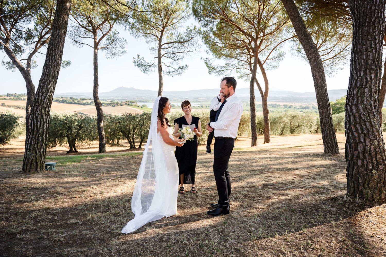 Elopement Photographer in Umbria. Couple exchanges vows outdoors under pine trees with scenic Tuscan landscape