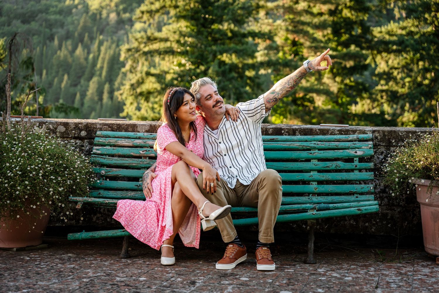 A couple shares a romantic moment on a green park bench surrounded by lush greenery in an outdoor setting.