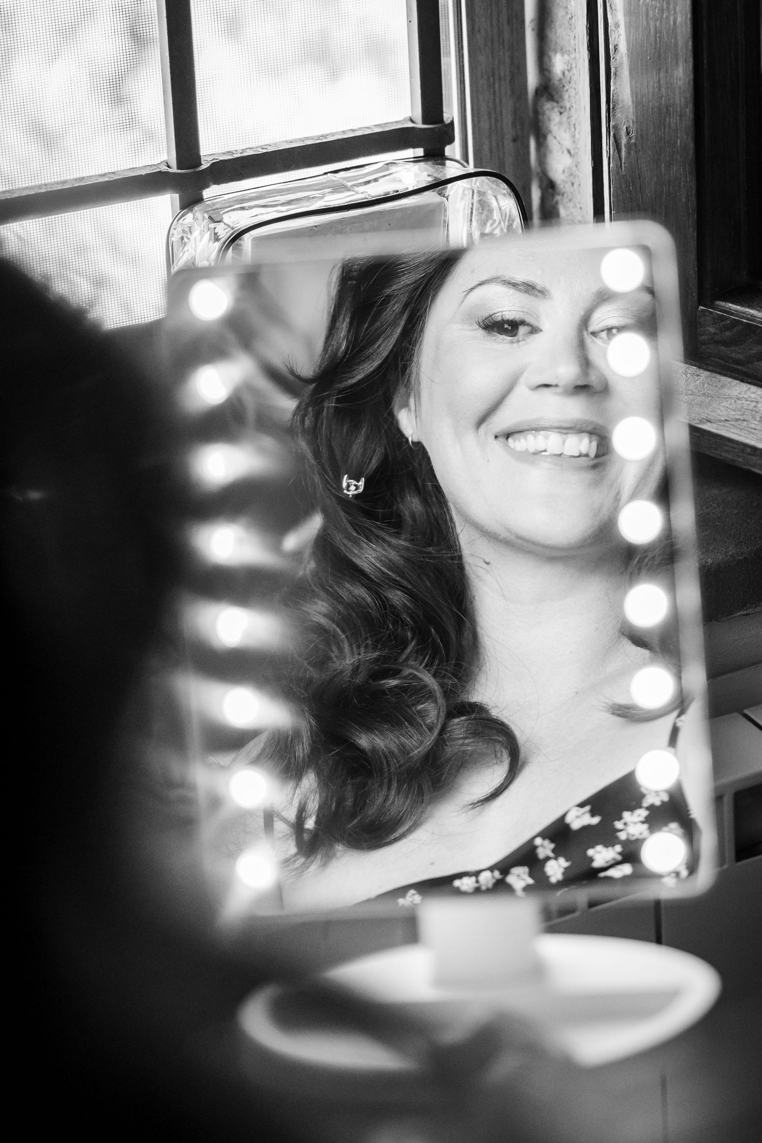 Black and white reflection of a smiling face in a mirror with bokeh light effects.