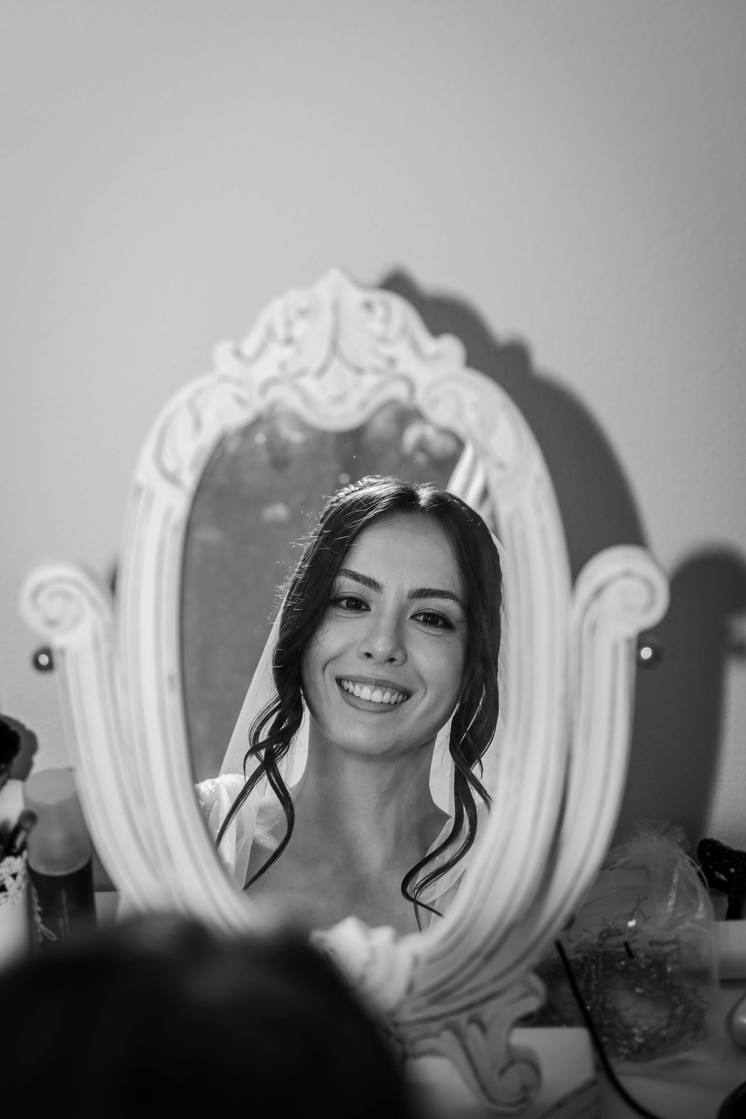 Smiling bride with tiara reflected in ornate white mirror in black and white wedding portrait.