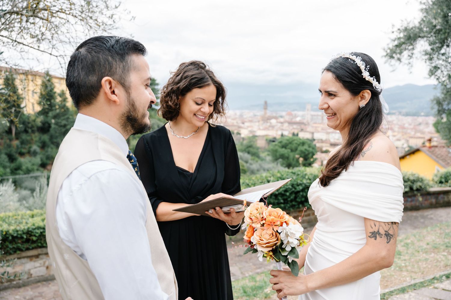 A couple shares an intimate moment outdoors while holding a bouquet of peach-colored flowers at sunset.