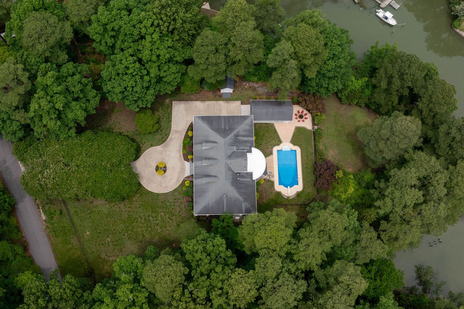 Aerial view of suburban home with pool surrounded by lush green trees near waterway.
