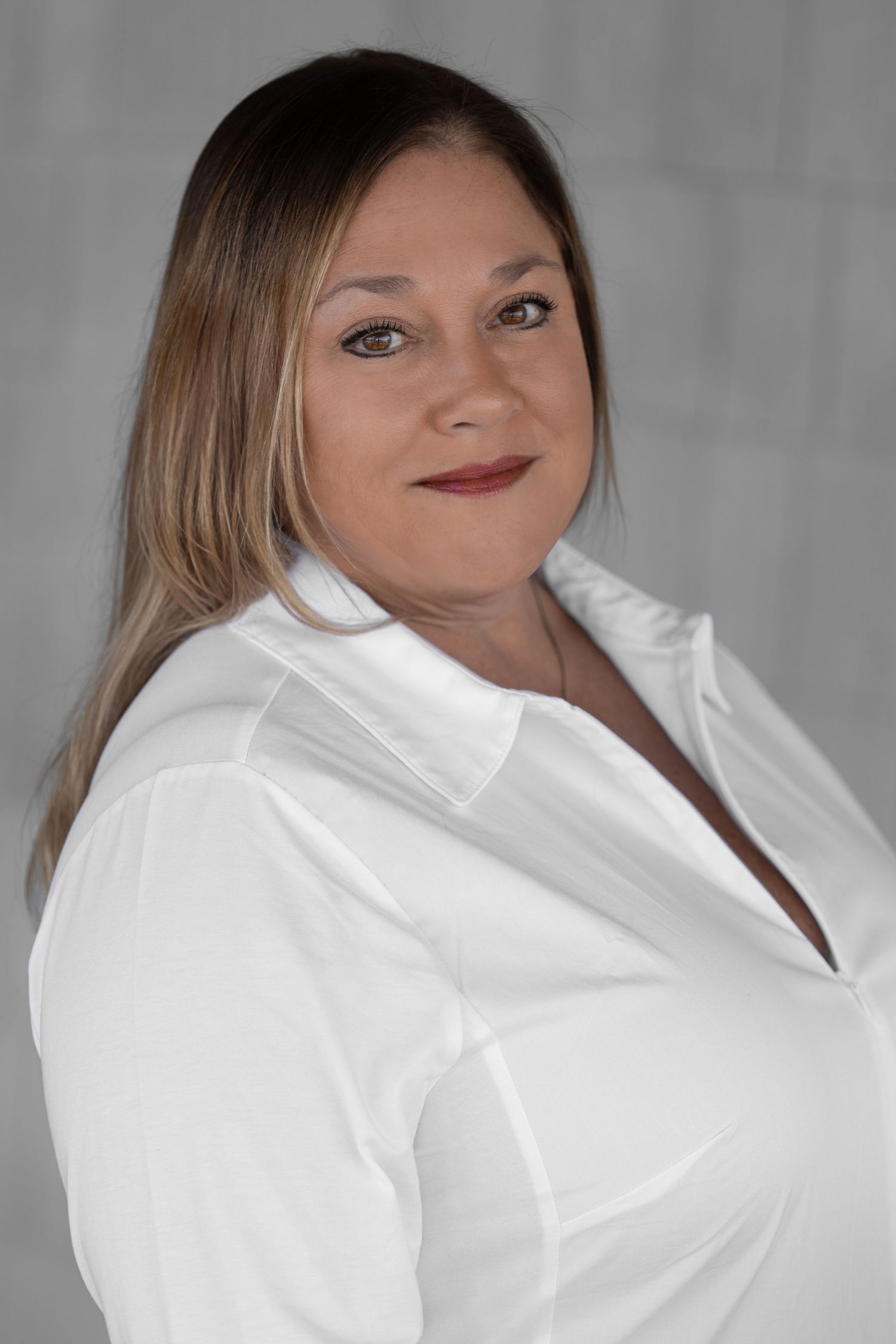 Professional woman with blonde hair wearing a white button-up shirt, smiling confidently against a gray background.