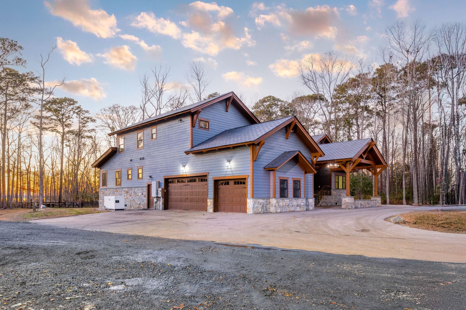 Rustic craftsman-style home with stone accents, double garage, and wood trim set among tall trees at sunset.
