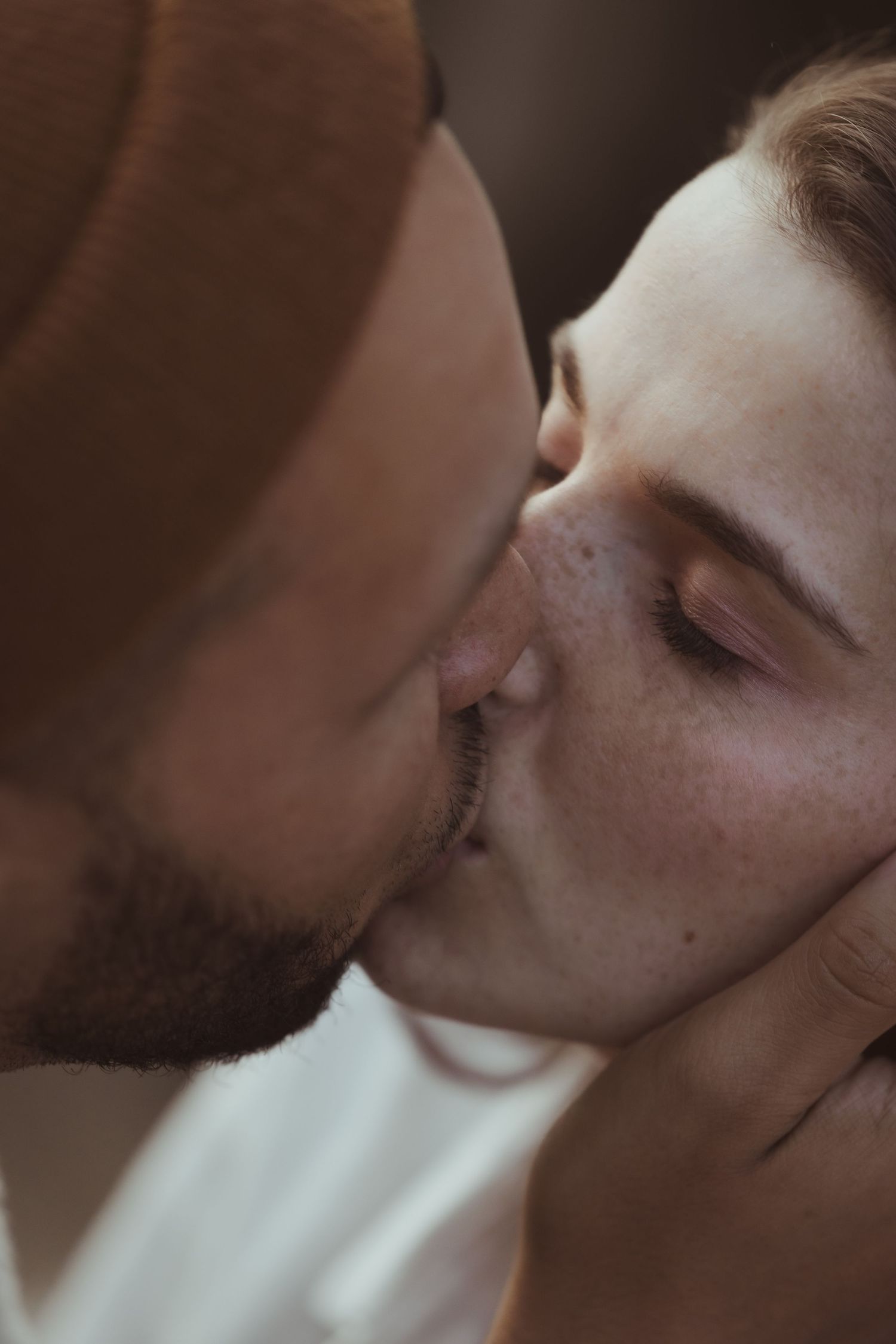 Close-up of a bearded man and freckled woman sharing a tender kiss.