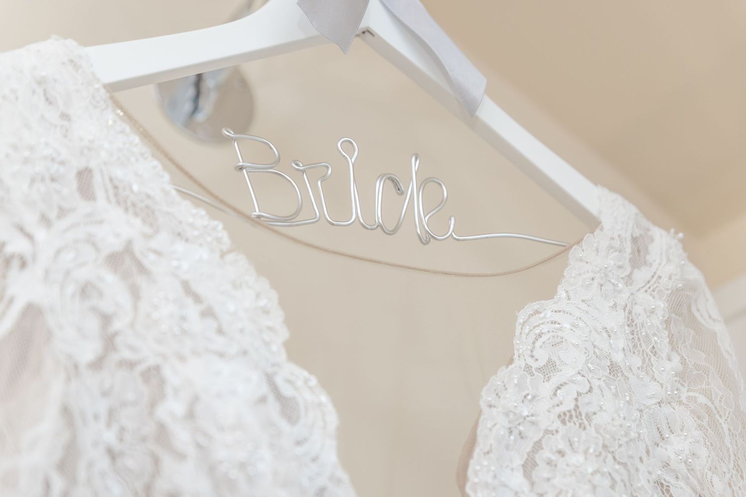 White lace wedding dress hanging on a hanger with decorative wire Bride label for bridal preparation.