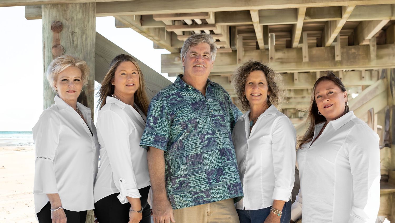 Five professionals posing together under a beach pier, with ocean views in the background.