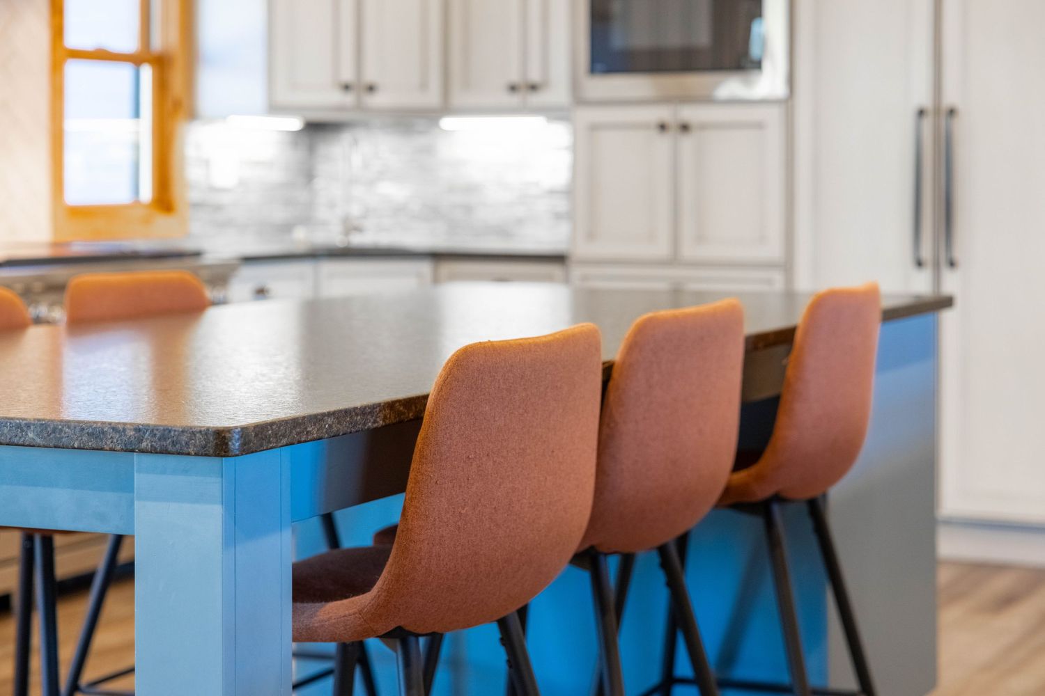 Modern kitchen island with blue base, granite countertop, and orange leather bar stools in bright white kitchen.