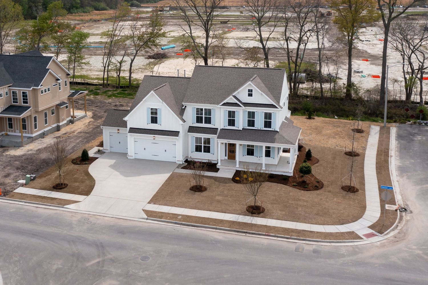Aerial view of newly built two-story white craftsman home with attached garage in developing neighborhood.