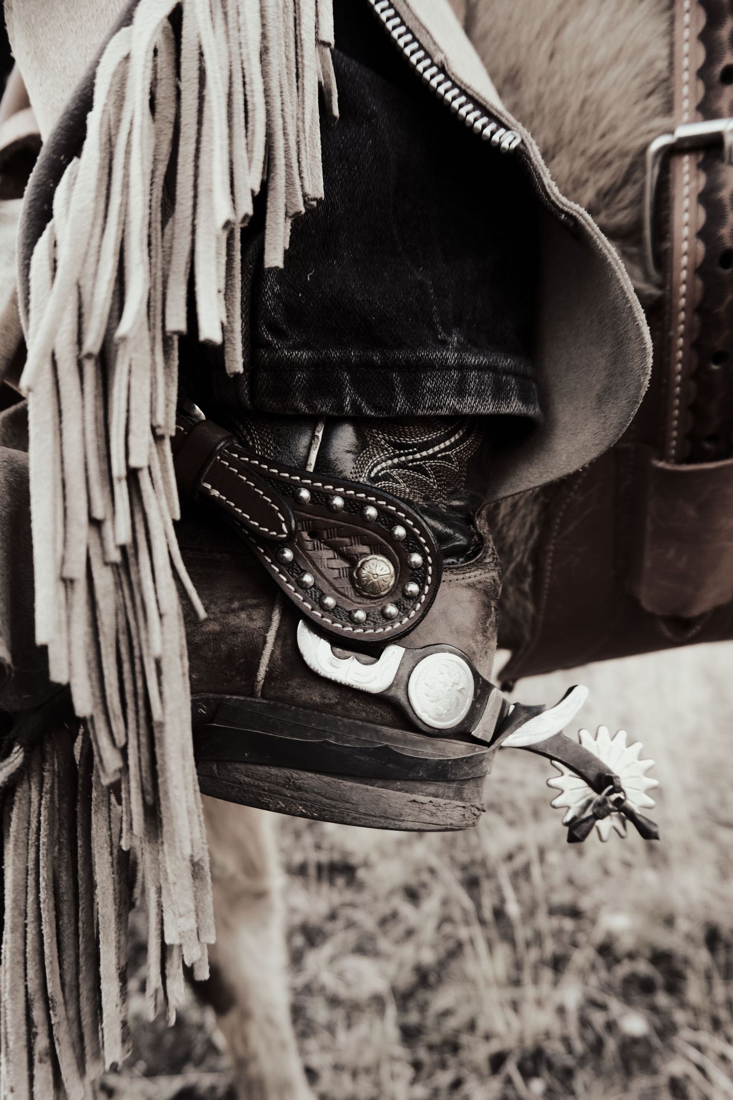 Close-up of a western boot with spurs and leather fringe details in black and white.