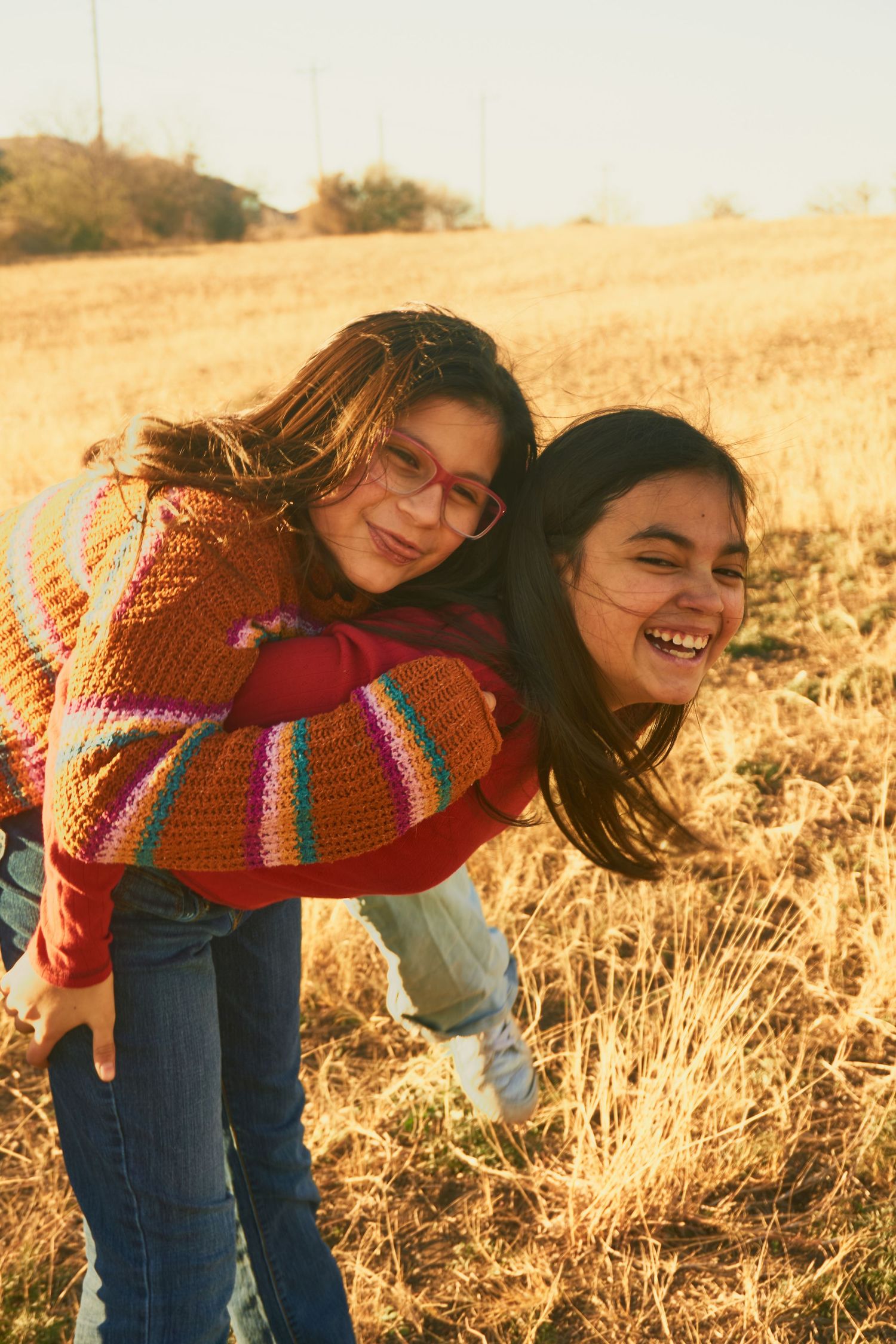Two friends enjoying a playful piggyback ride in a golden field during sunset.