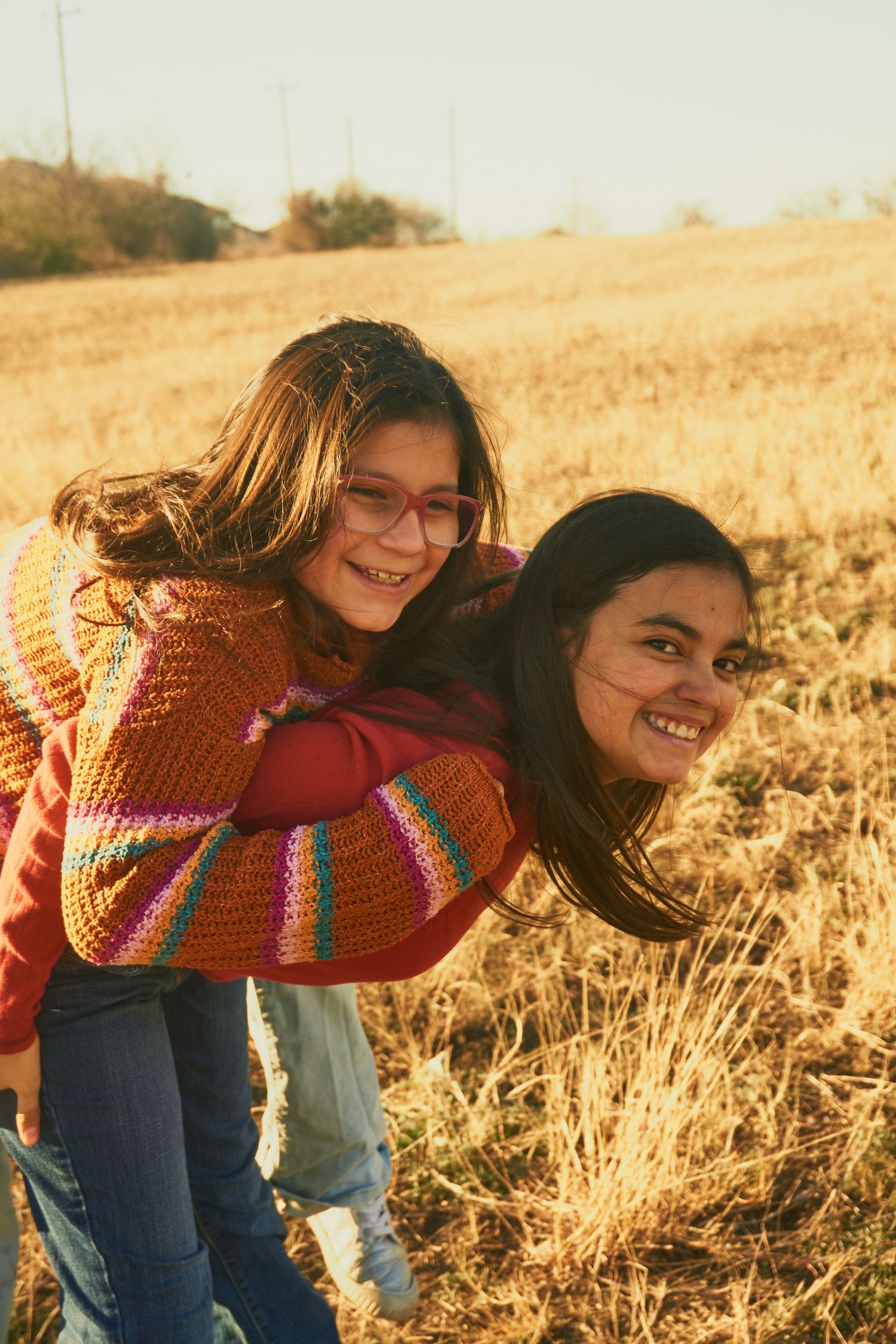 Two friends sharing a playful moment in a golden wheat field at sunset.