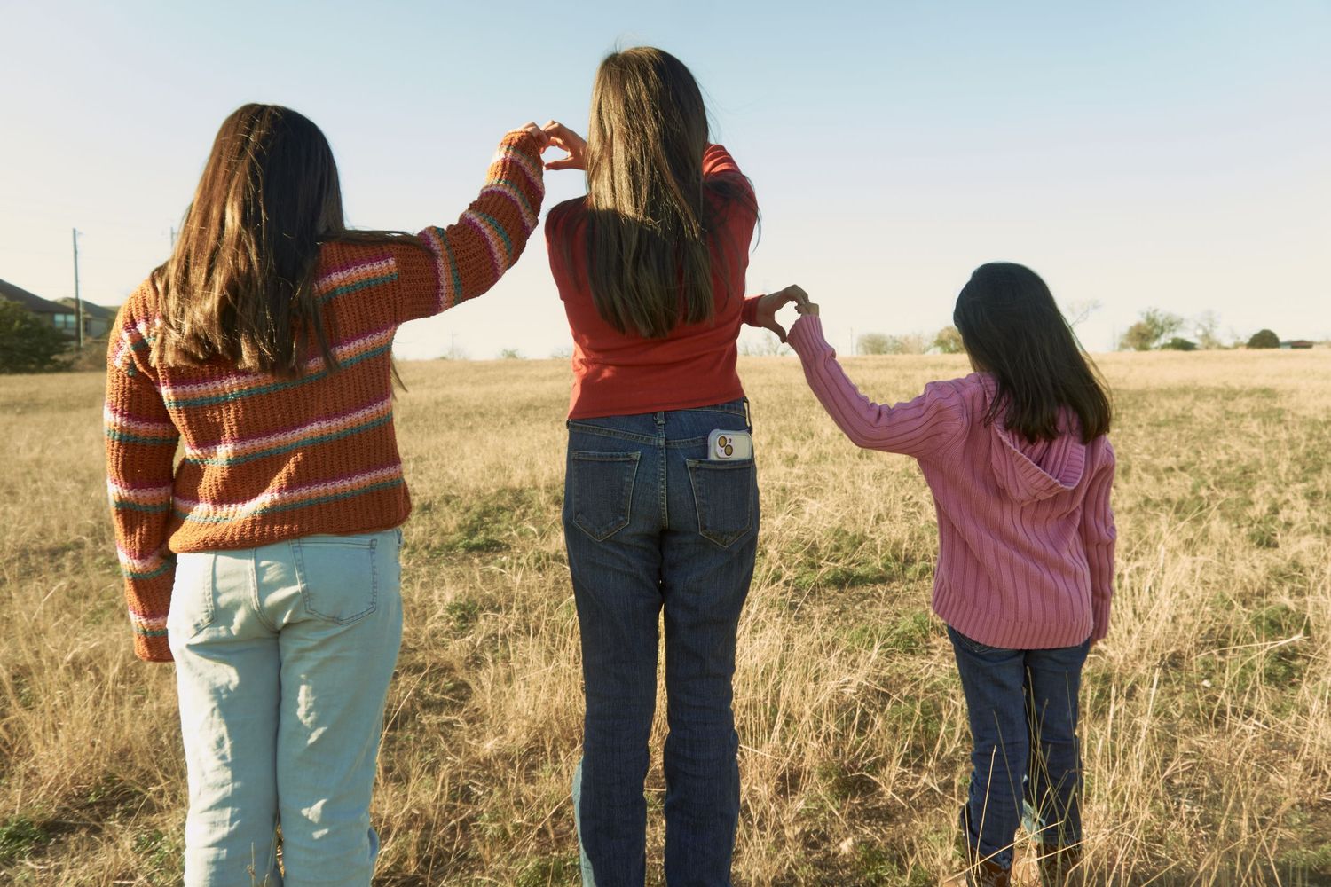 Three people hold hands while walking through a golden field at sunset.