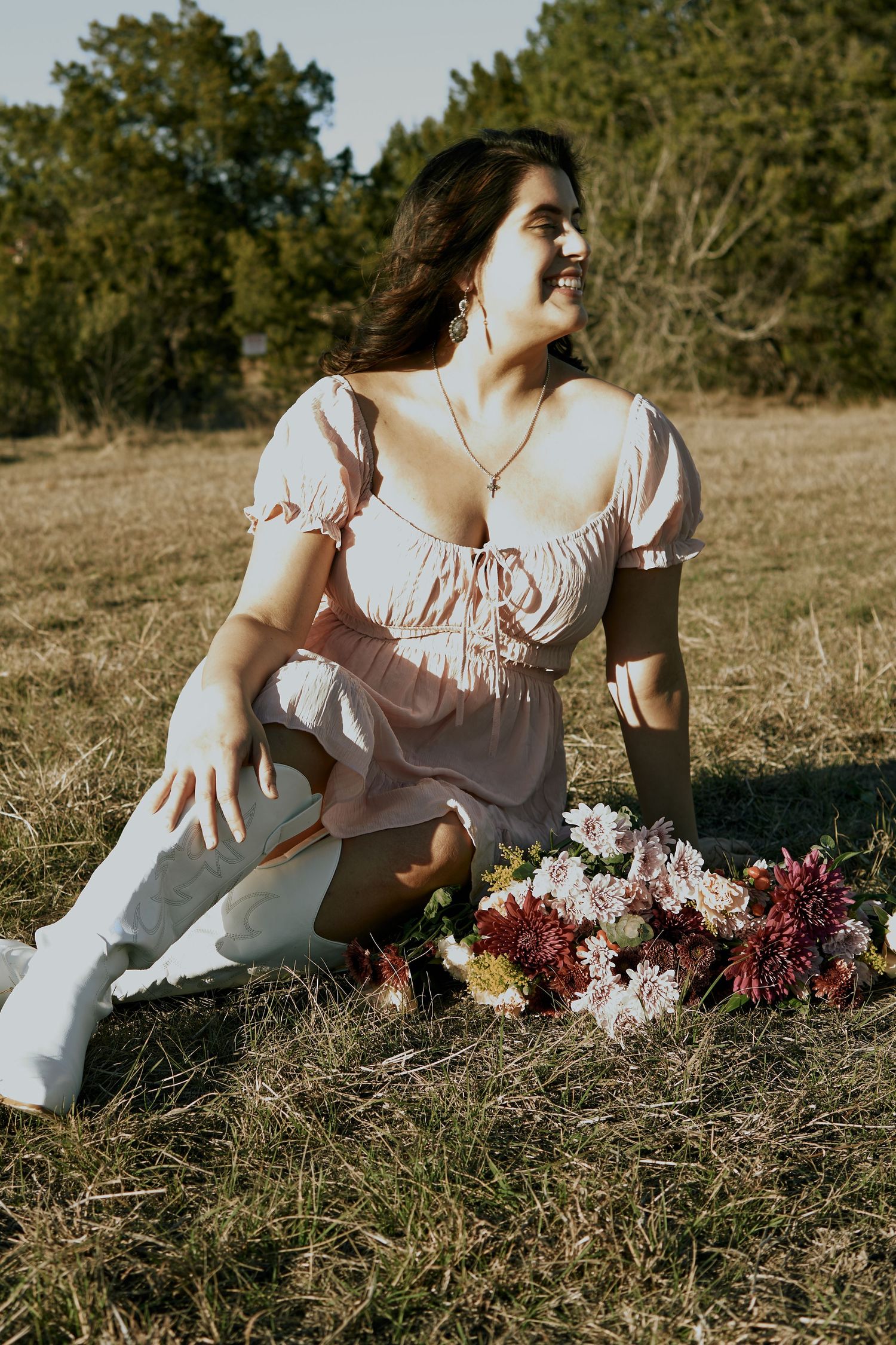 A person in a romantic dress sits in a field next to a colorful flower arrangement.