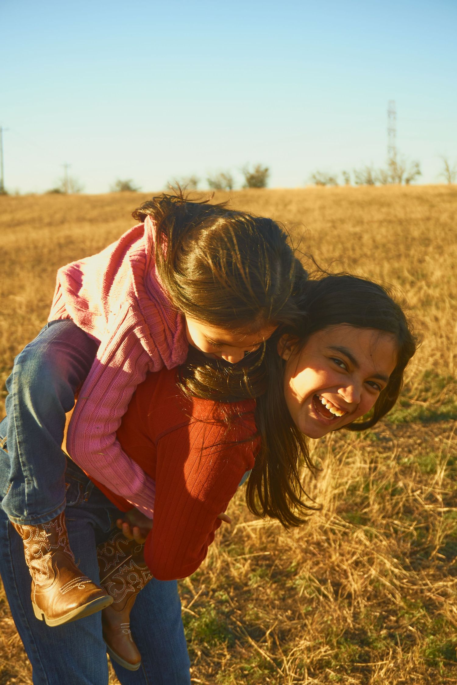 Friends sharing joyful piggyback moment in a sunlit field.