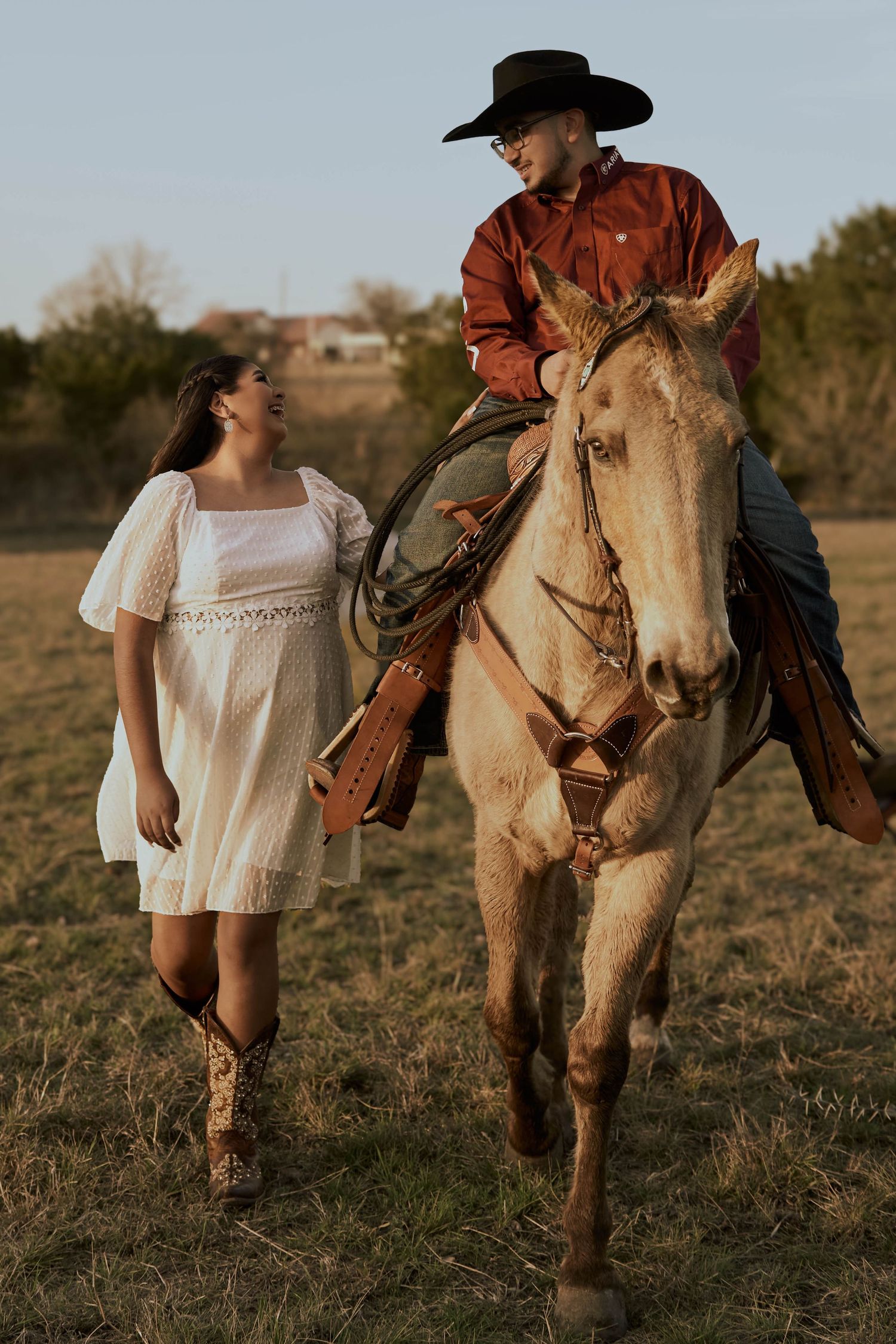 A couple shares a romantic moment in a field as she walks beside his pale horse at sunset.