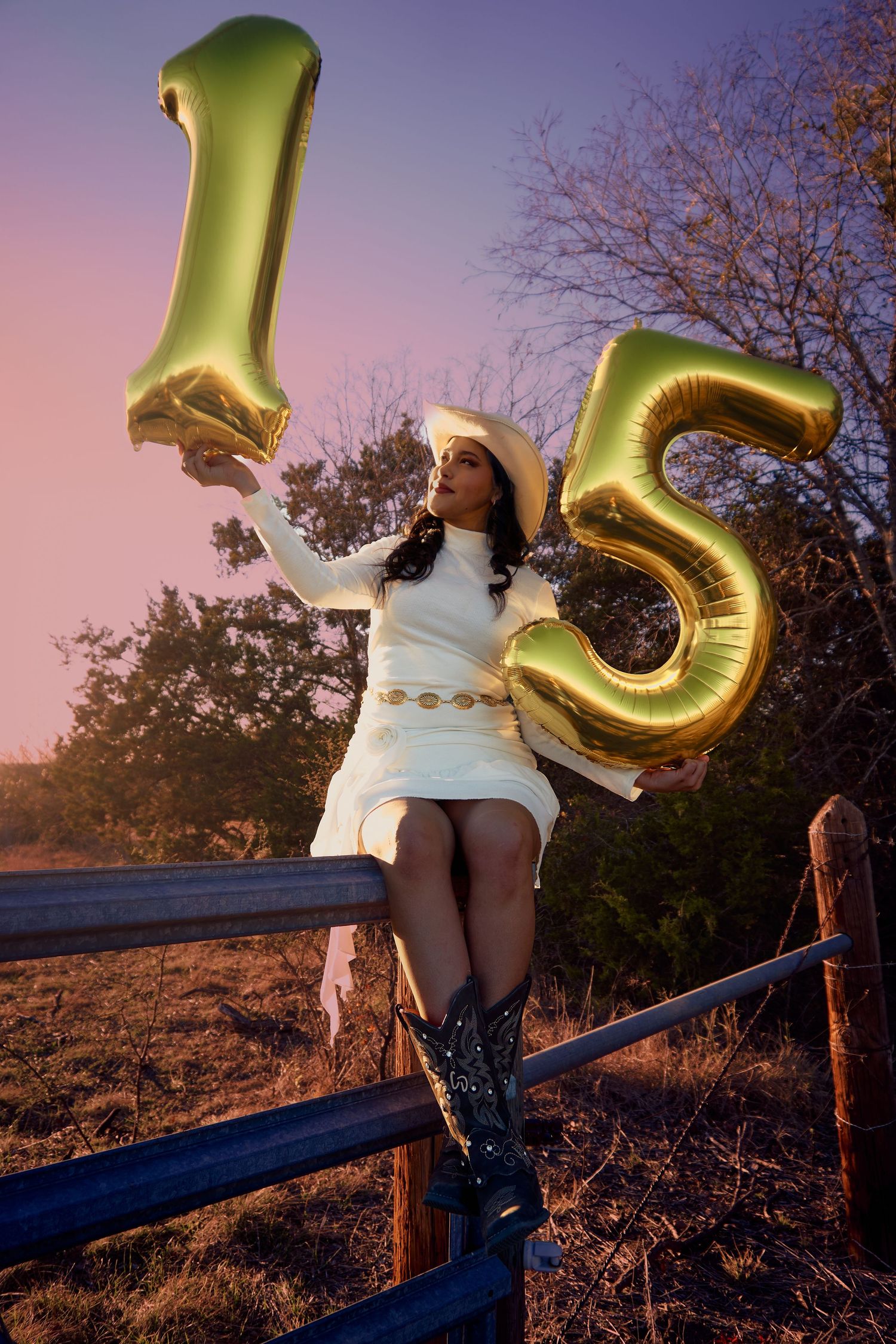 Celebratory scene with gold number 15 balloons at sunset against rustic fence.