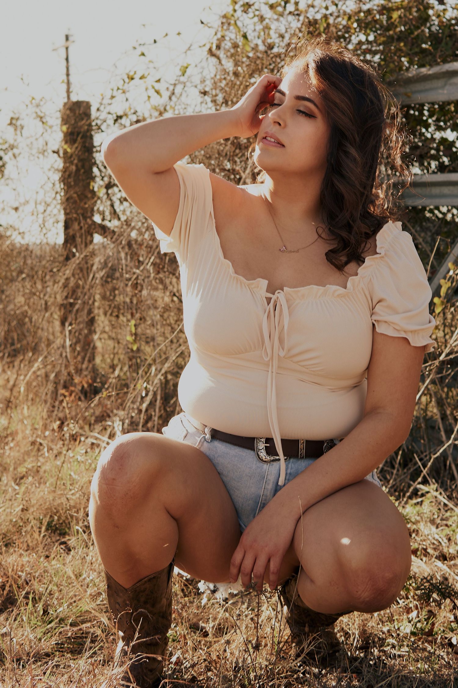 Casual portrait in cream top and denim shorts against rustic fence at golden hour.